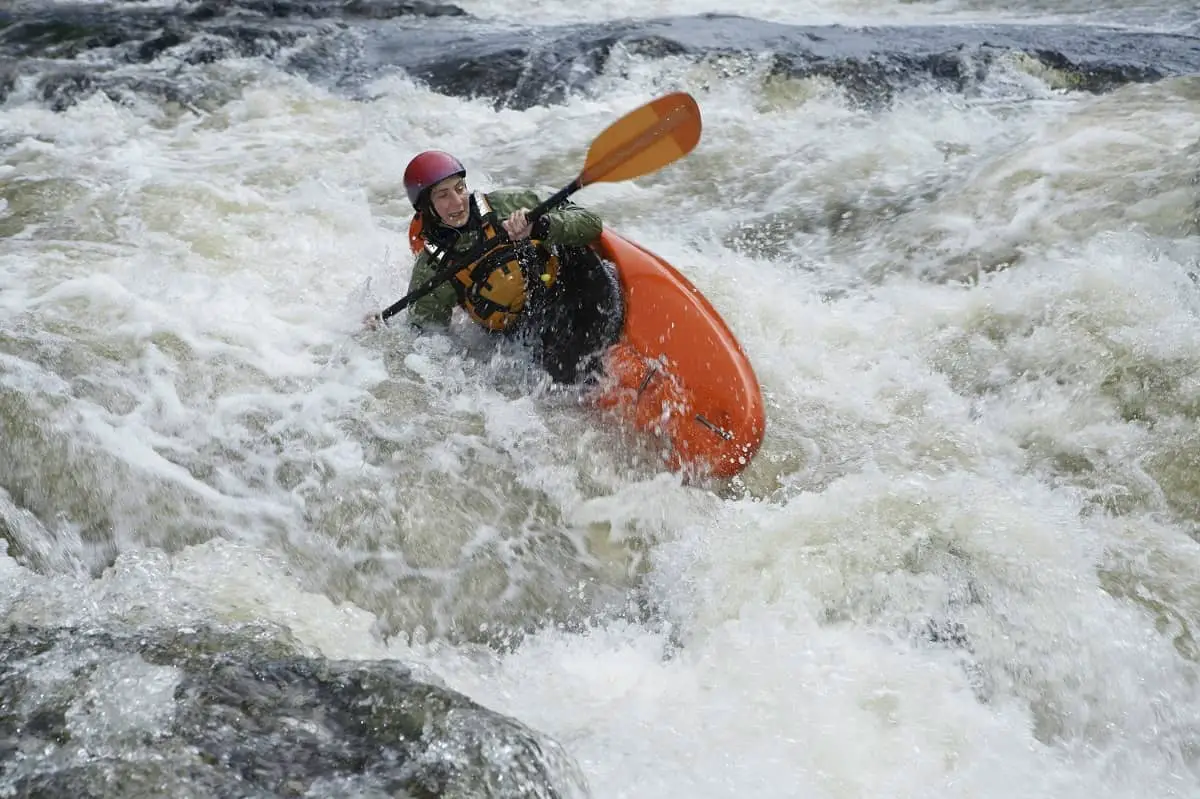 Woman wearing safety jacket and water sports helmet in kayak tipping over in rapids