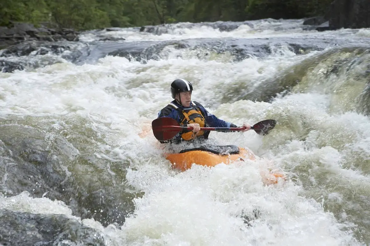 Man kayaking in whitewater rapids wearing safety jacket and water helmet