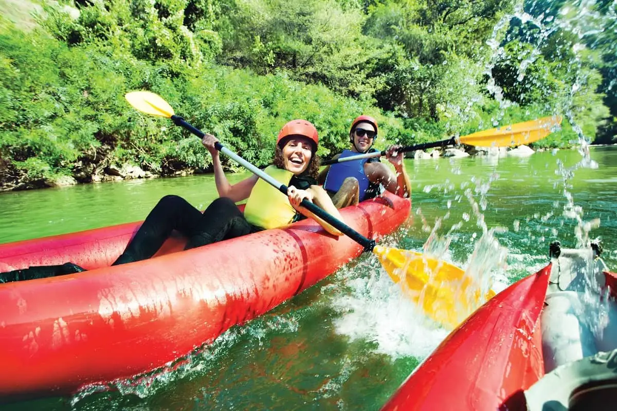 couple paddling in a canoe wearing orange water sport helmets