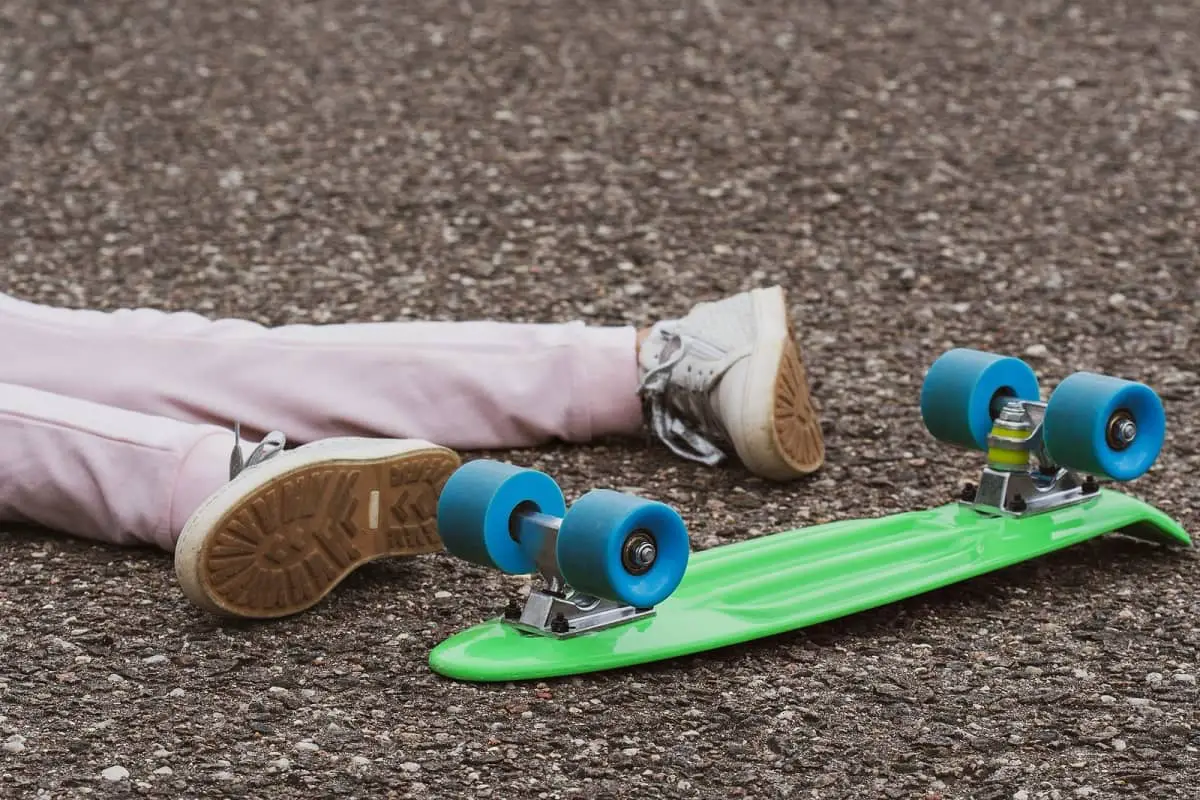 Child lying on ground next to overturned skateboard