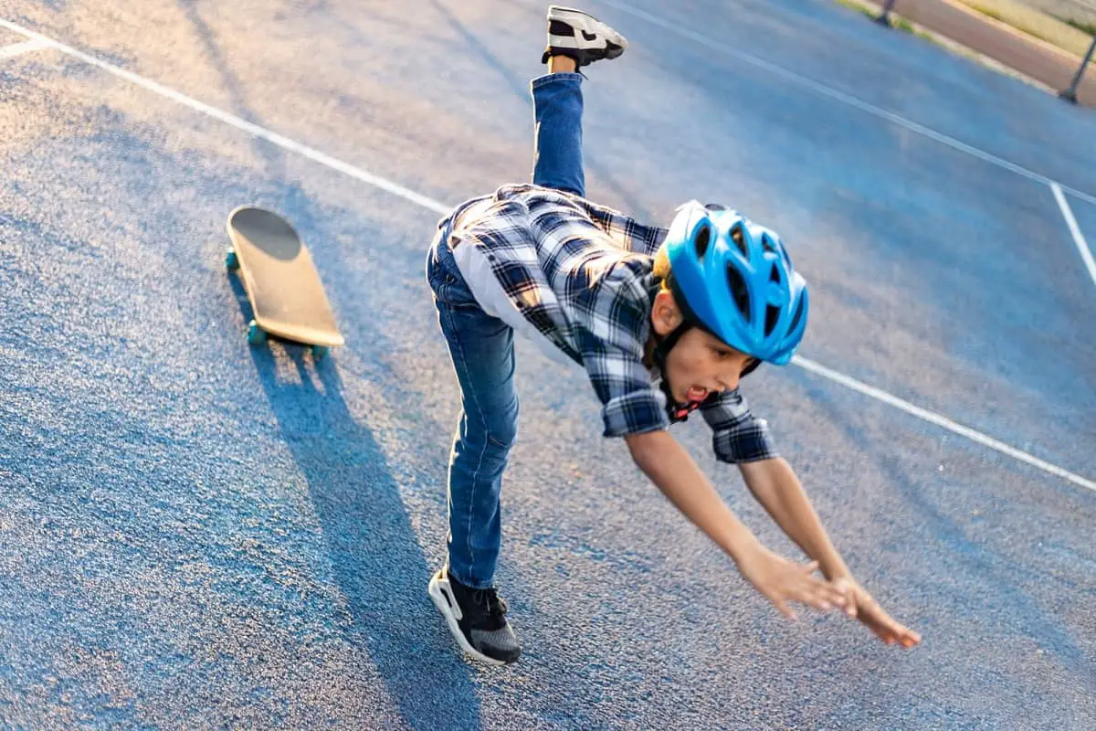 Boy wearing bicycle helmet falling from skateboard