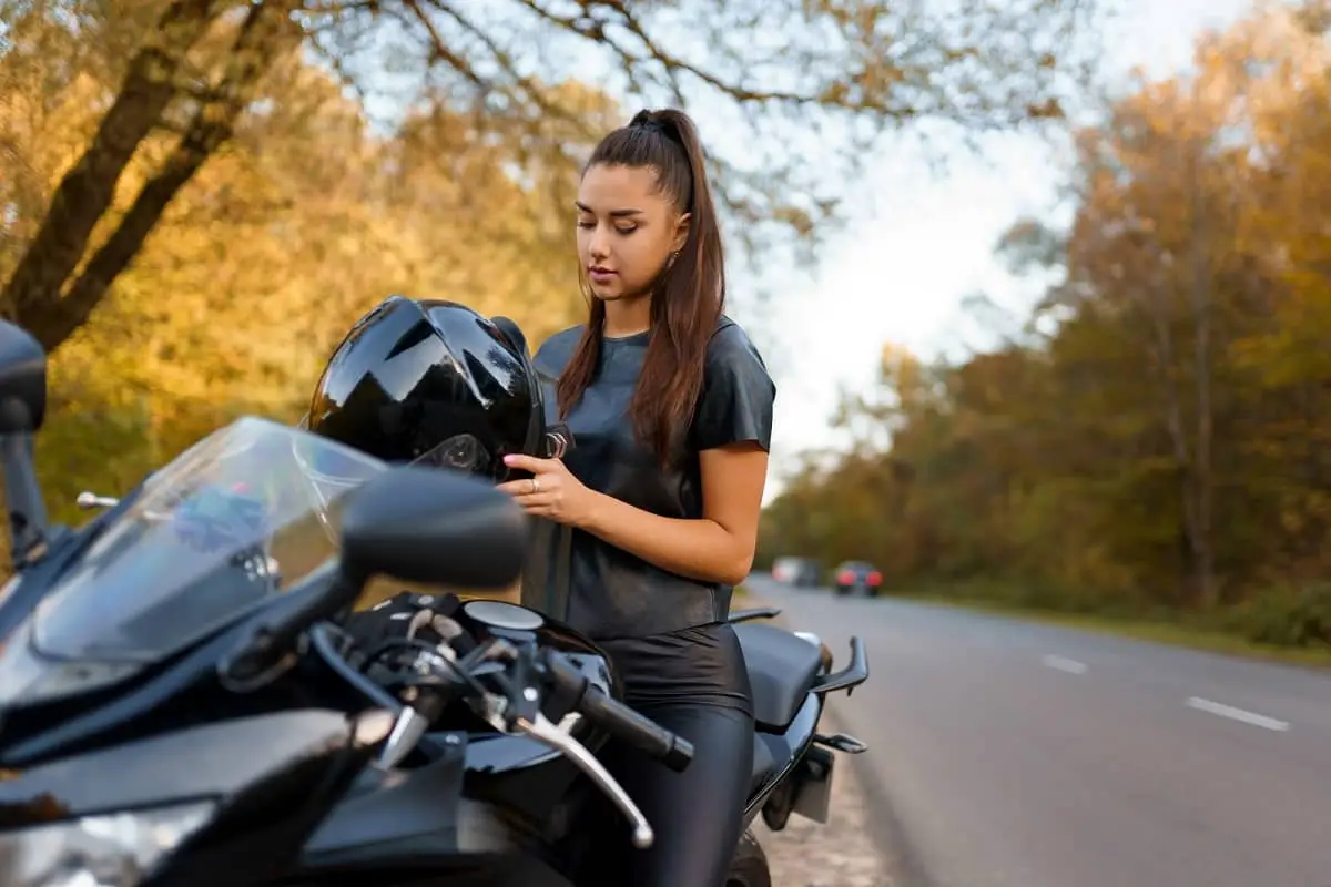 Woman sitting on motorcycle holding helmet