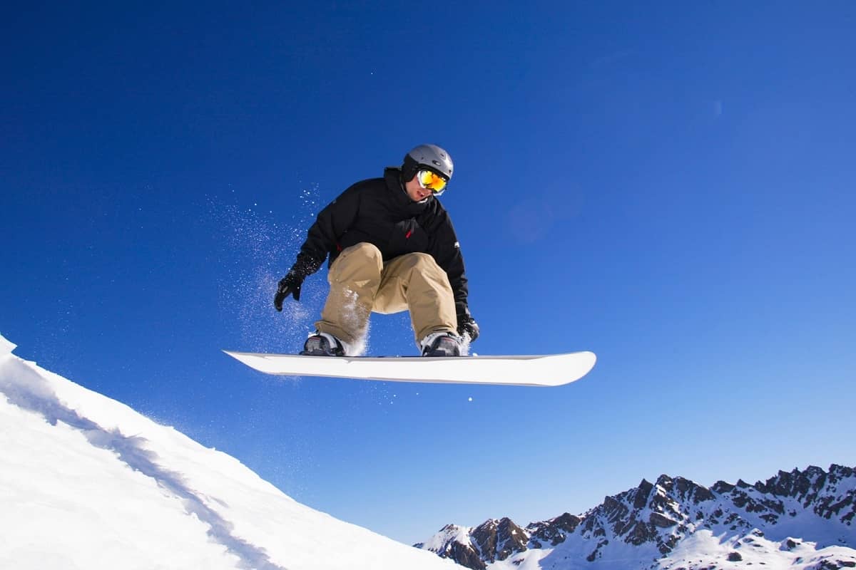 Snowboarder mid-flight wearing a helmet with clear blue sky. Hard to say is he's wearing a mips ski helmet or not!