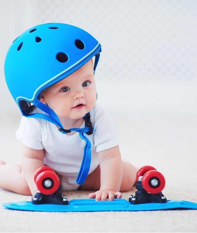 Baby wearing over-sized skateboard helmet sitting on floor with skateboard