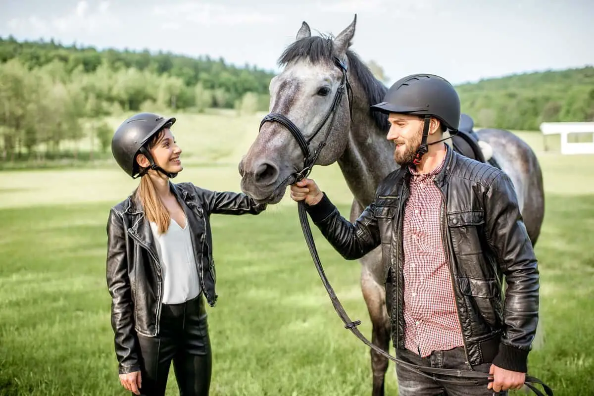 Man and woman wearing helmets standing with horse.