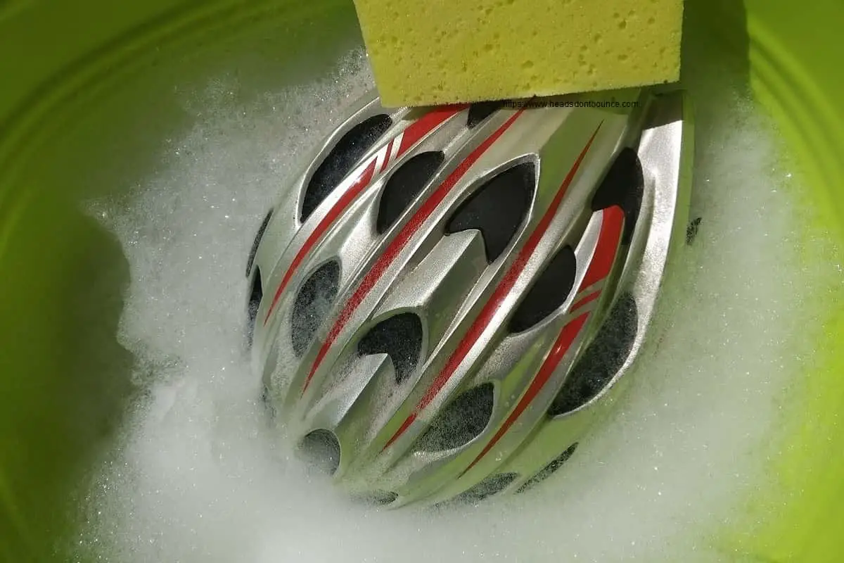 Silver and red bicycle helmet in soapy water with yellow sponge