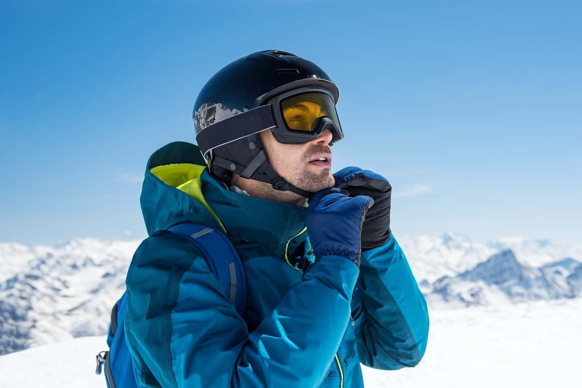 man adjusting chin strap of black ski helmet