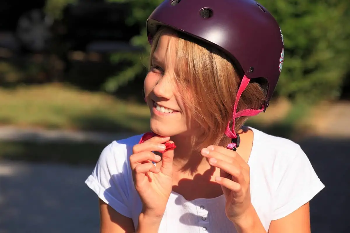 Teenage girl fastening chin strap on skateboard helmet