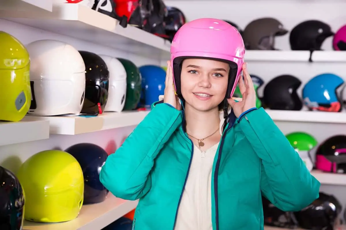 How should a ski helmet fit?  This teenage girl is trying on a pink ski helmet for the right fit.