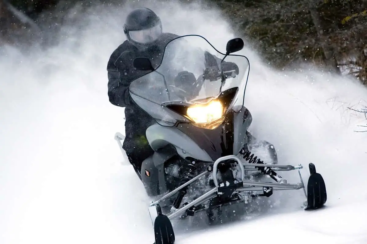 How to keep snowmobile helmet from fogging would be useful for this black snowmobile with headlight on driven by man wearing black clothes and helmet