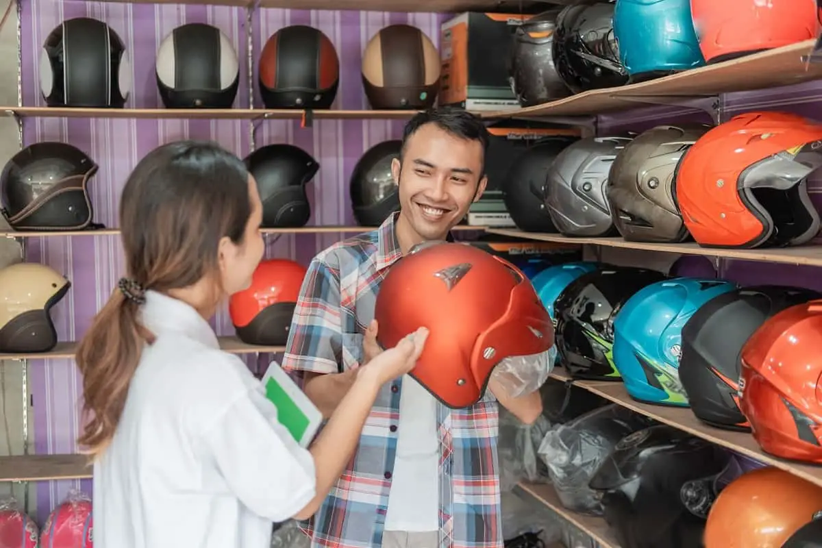 Salesgirl selling motorcycle helmet to man with shelves of helmets behind