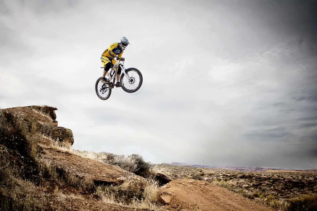mountain biker wearing full face helmet flies over jump in desert