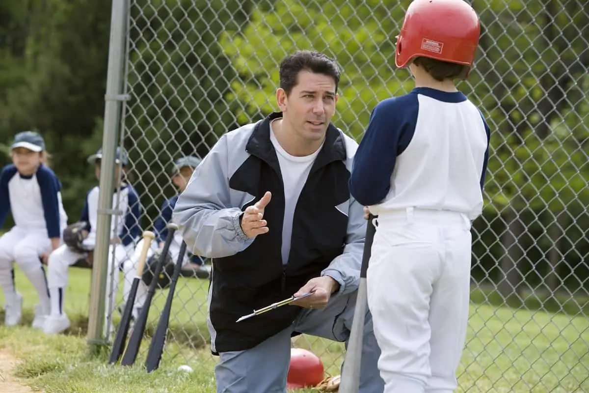 Baseball coach talking to young player wearing red baseball helmet