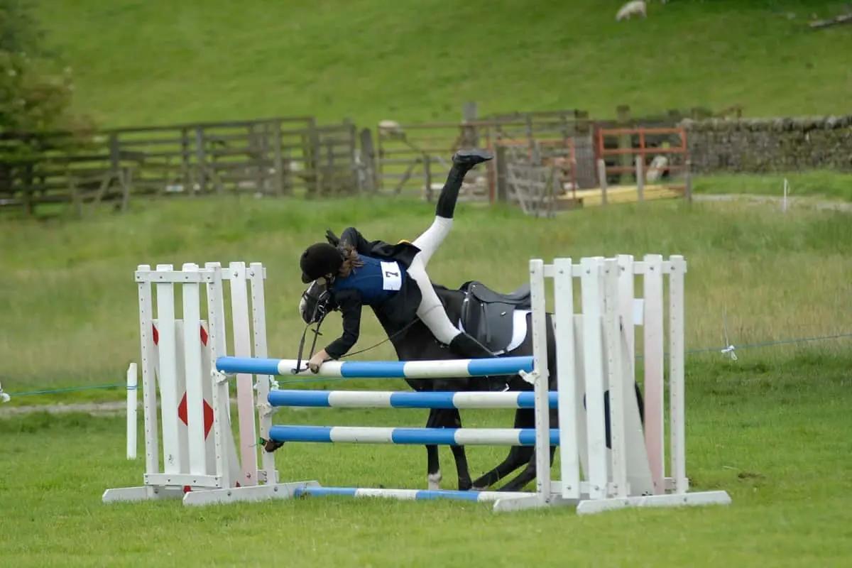 female horse rider falling from horse at a jump