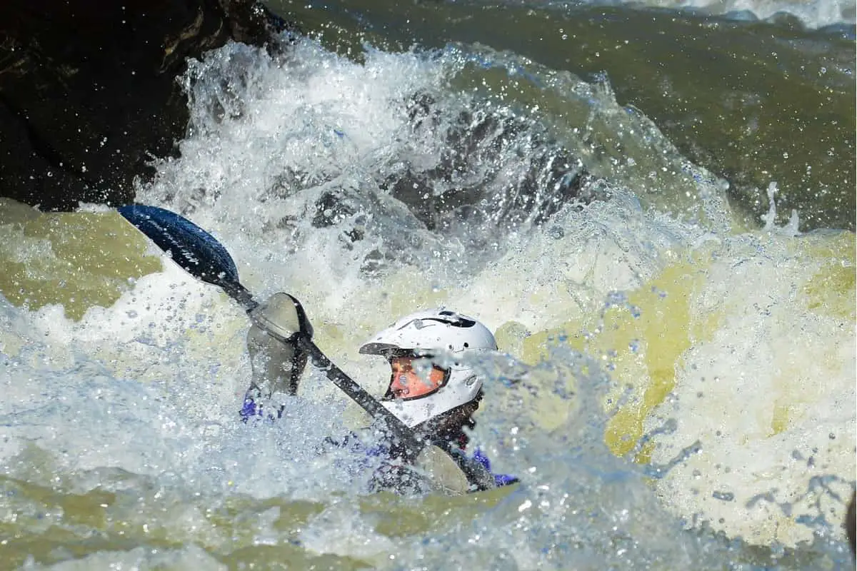 Man wearing full-face kayak helmet in rough rapids