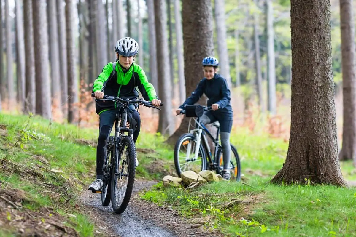 Two girls riding bikes in the woods along a narrow trail