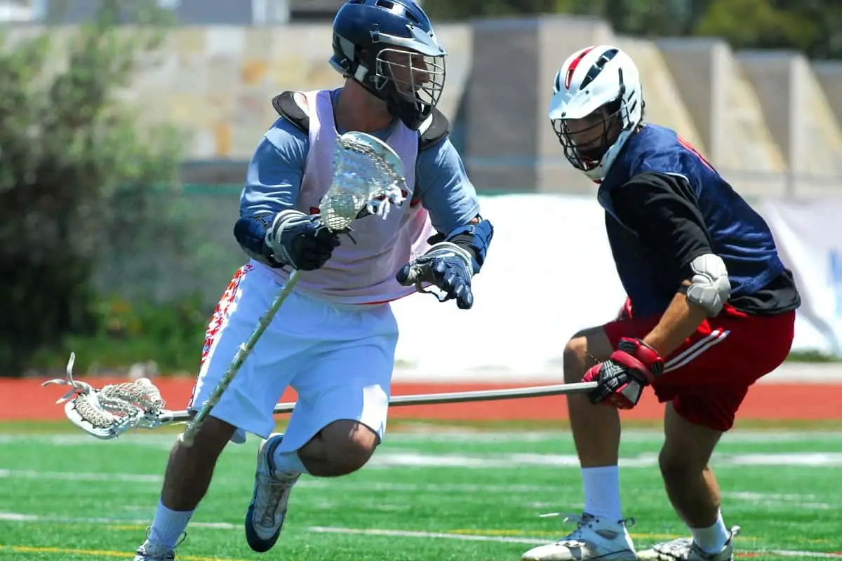 Lacrosse game in progress. One player has ball while being tackled by opponent.