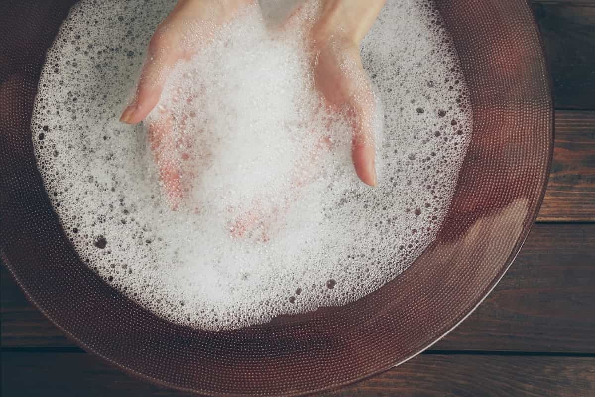 pair of hands in bowl of soapy water