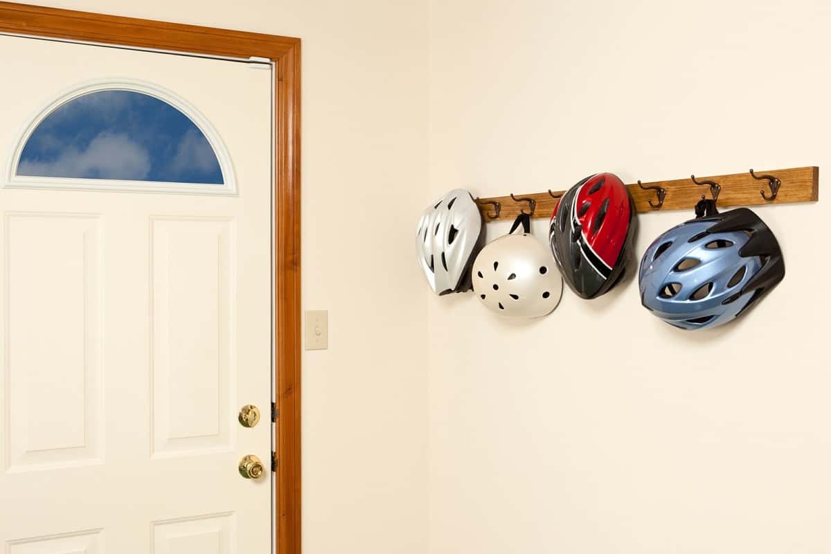 4 bicycle helmets hanging on hooks inside a doorway
