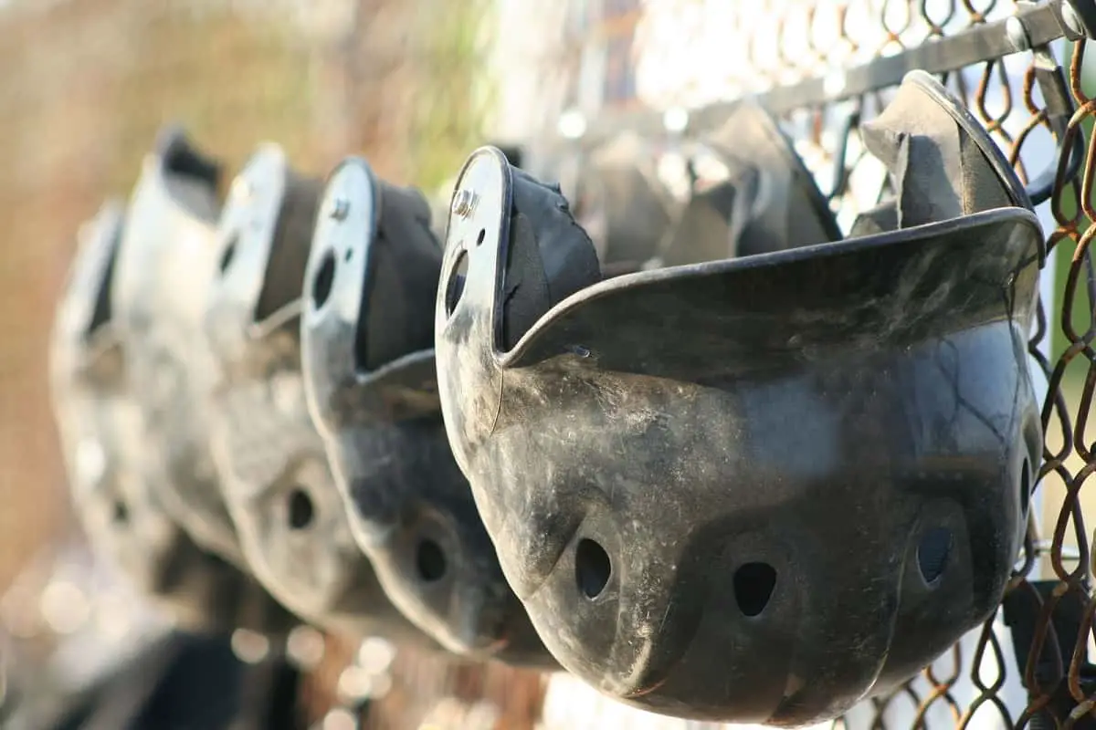 Old battered baseball helmets hanging on a wire mesh fence
