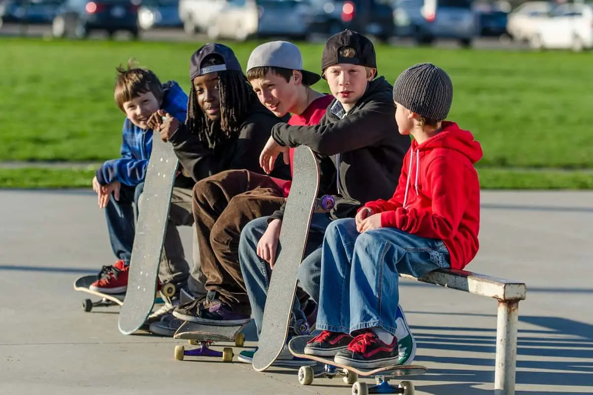 five young boys sitting on a bench with their skateboards without helmets