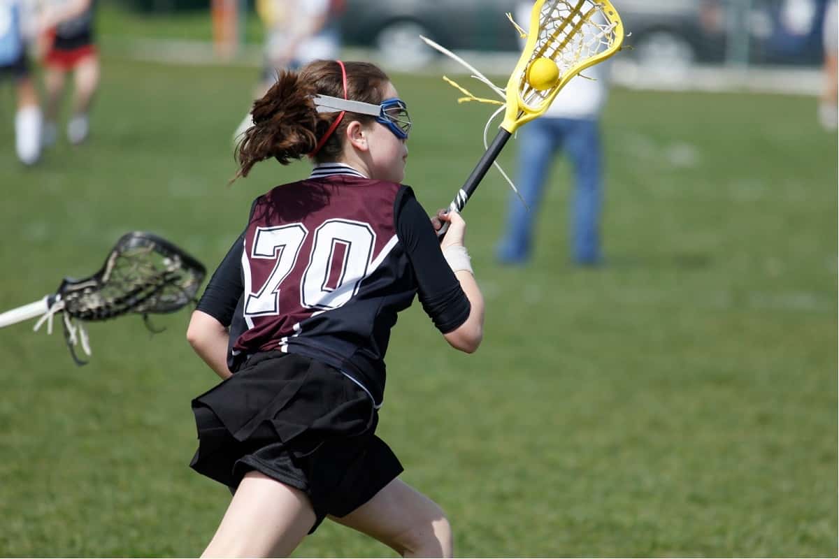 girl lacrosse player running with ball and stick while wearing goggles