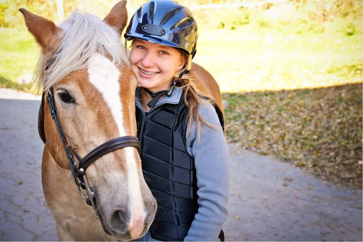 teenage girl with braces on her teeth wearing a new riding helmet standing by her horse