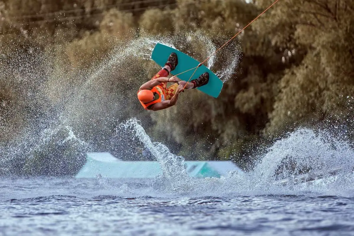 wakeboarder in the air upside down after going over a jump, wearing an orange helmet