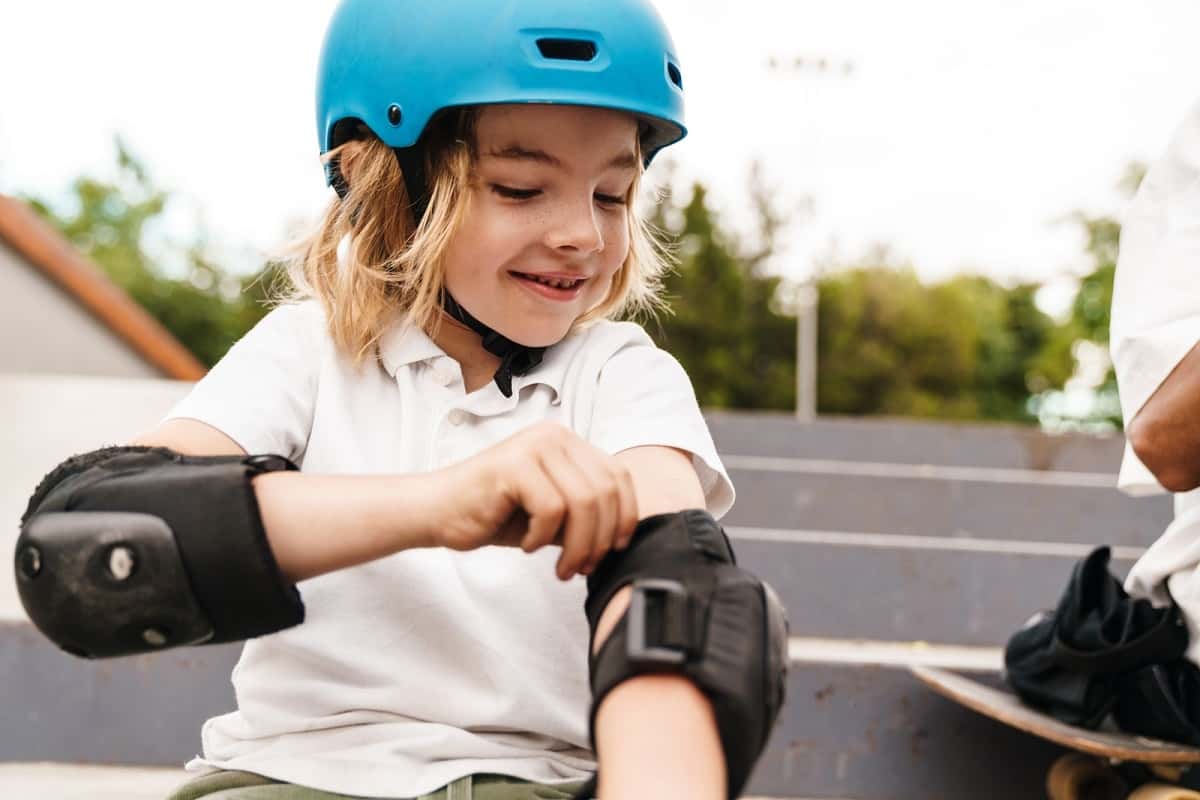 young girl wearing a blue skateboard helmet putting on elbow pads