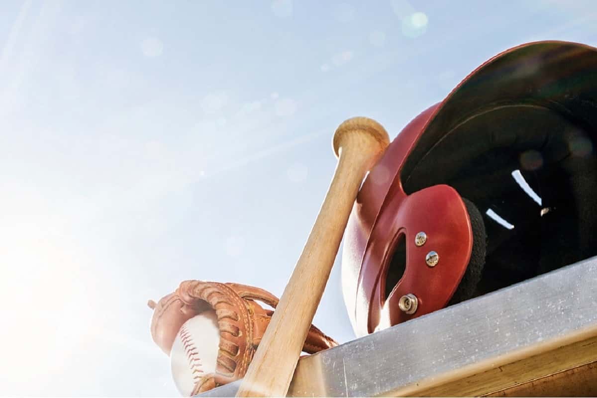 baseball catchers mitt with baseball, baseball bat and red batters helmet on table