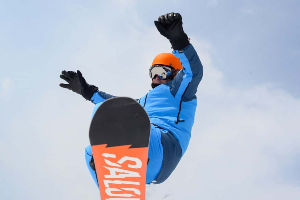 Can I Use a Snowboard Helmet for Wakeboarding? 4 man wearing blue snow suit and orange helmet on snowboard in mid air jump