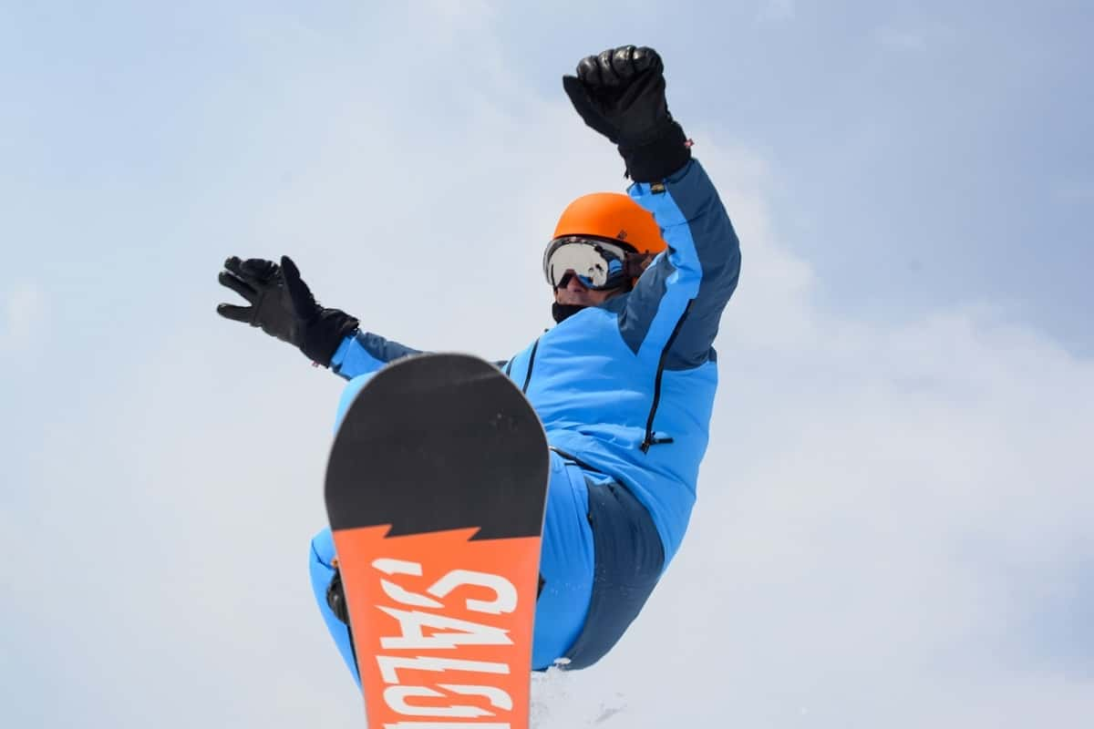 man wearing blue snow suit and orange helmet on snowboard in mid air jump