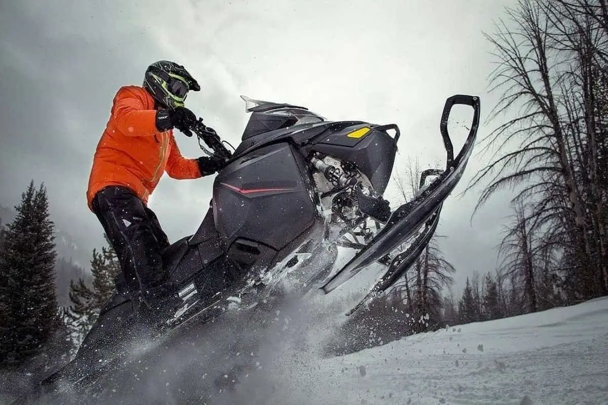 The best snowmobile helmet with heated shield worn by this man wearing an orange jacket and black helmet while riding his snowmobile.