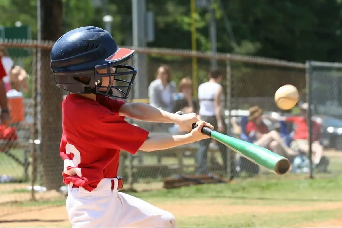 very small boy wearing helmet with face shield about to hit the baseball
