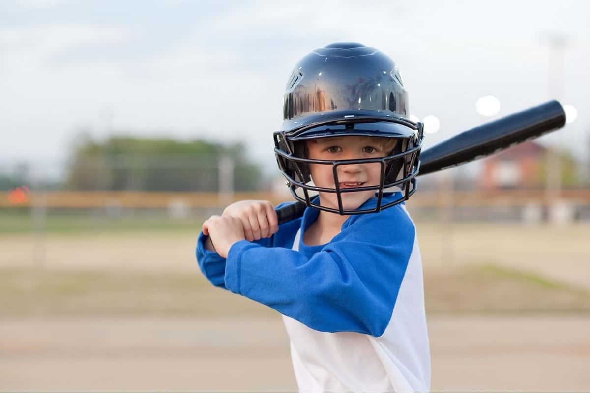 very young boy wearing black helmet with face shield holding baseball bat ready to hit ball