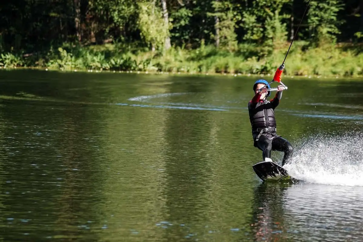 young person wearing all black wetsuit and blue helmet wakeboarding