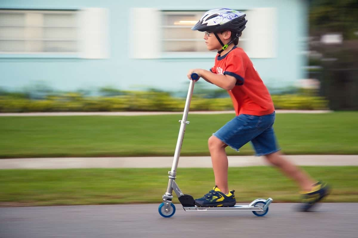 young boy riding a kick scooter while wearing a bicycle helmet