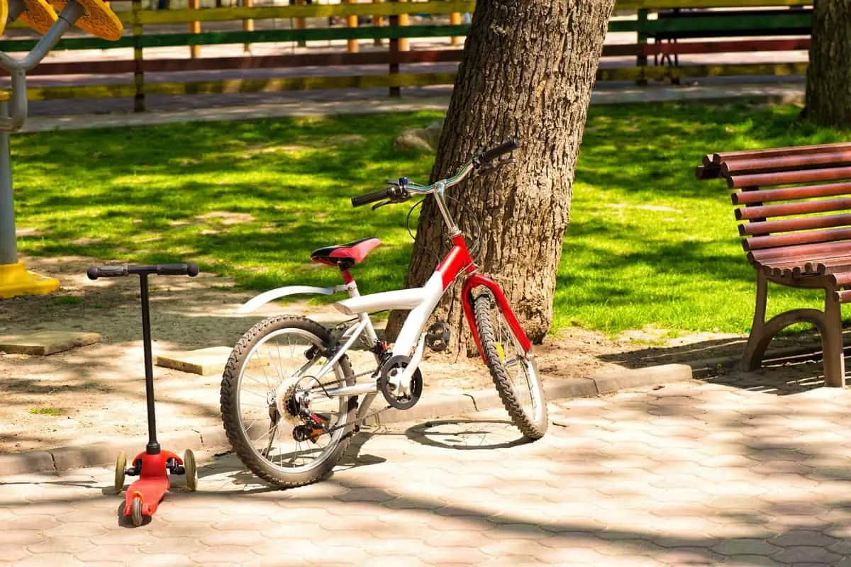 Scooter helmet Vs bike helmet: a child's scooter and bicycle in a park beside a large tree.