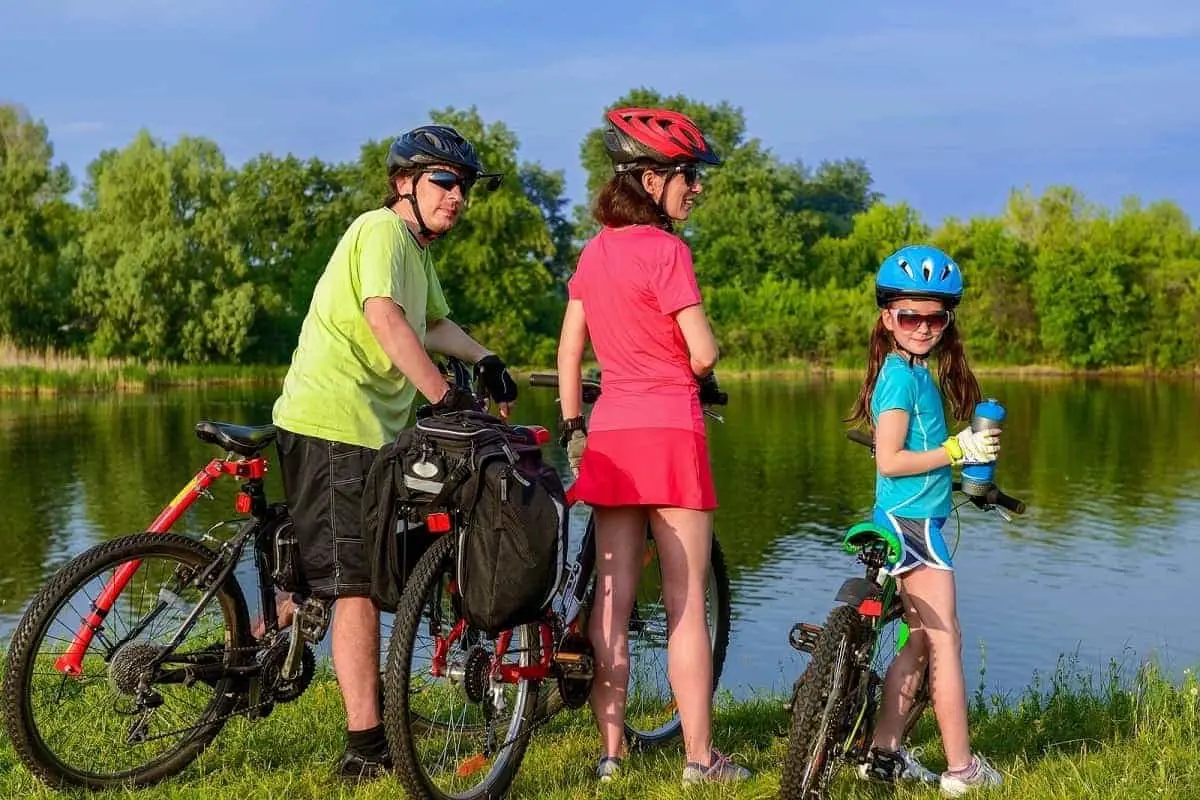 man, woman and child resting by a lake after cycling