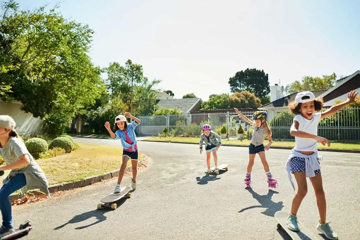 Five young girls with and without helmets skateboarding and rollerskating in the street