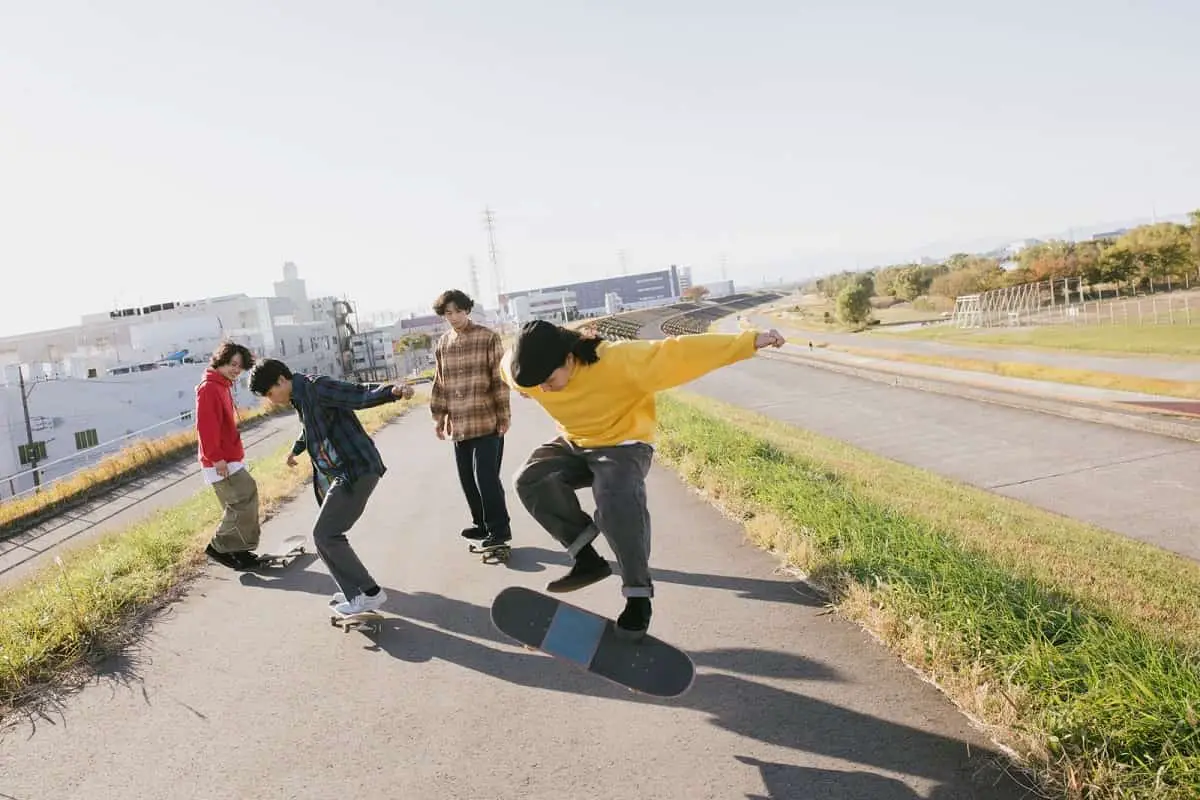 Four teenage boys on skateboards without helmets on a path doing tricks