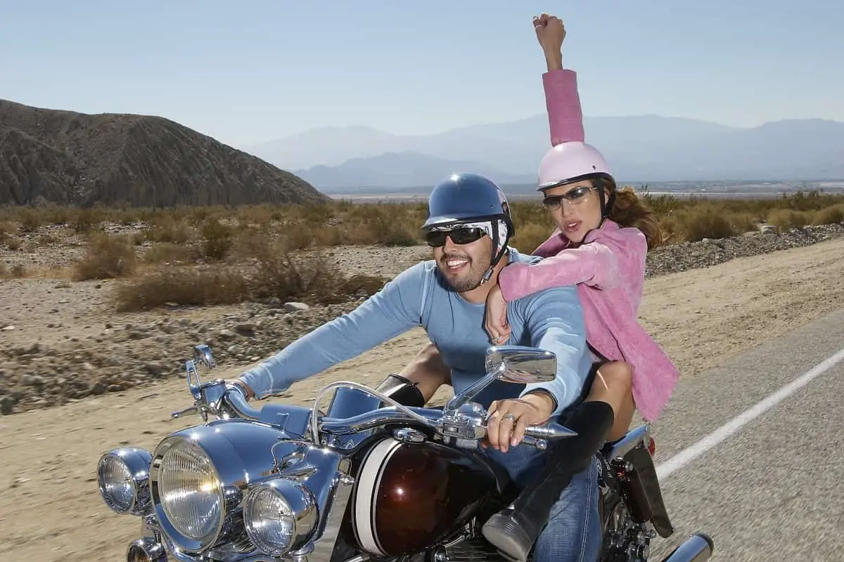 couple riding a motorcycle wearing small helmets