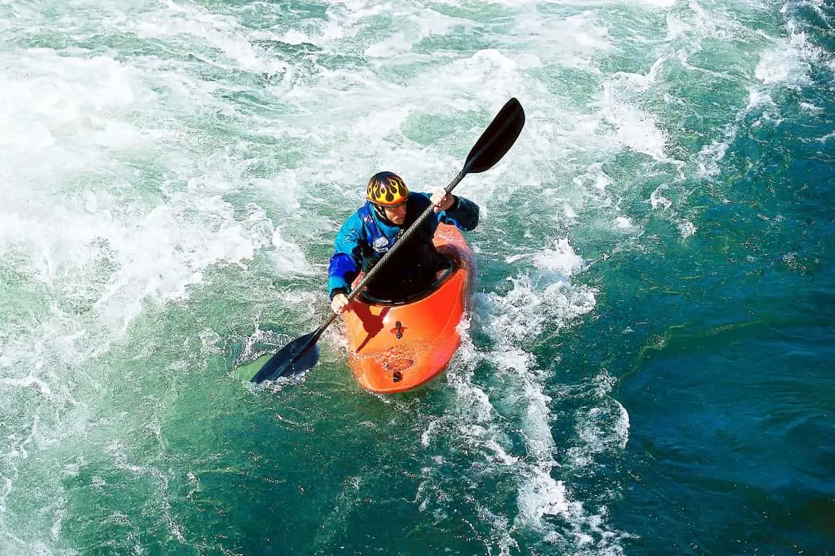 man in orange kayak in white water wearing an EN1385 certified watersports helmet