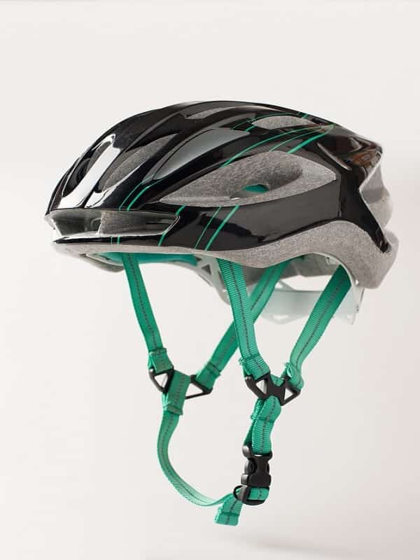 black bicycle helmet with green chinstrap hanging on wall