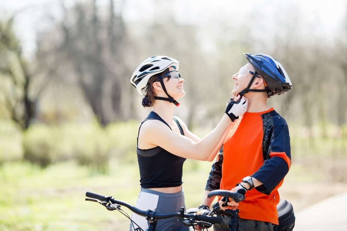 woman wearing white bike helmet adjusting helmet chinstrap for man