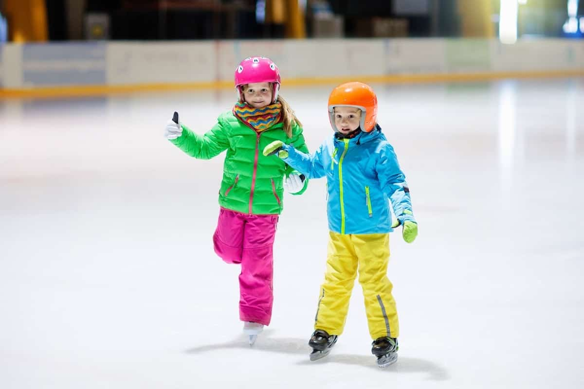 two young girls ice skating at the skating rink wearing helmets