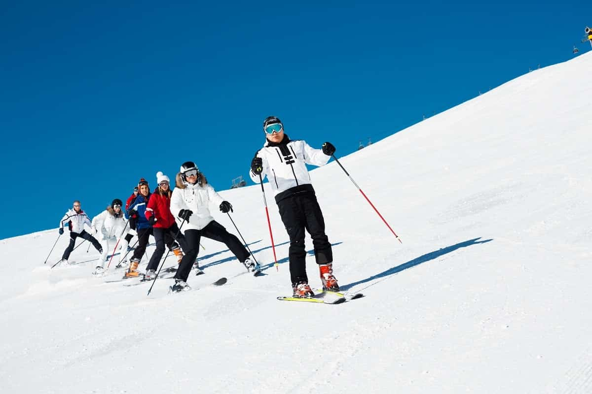 snow skiing class in single file snow plowing down a small slope