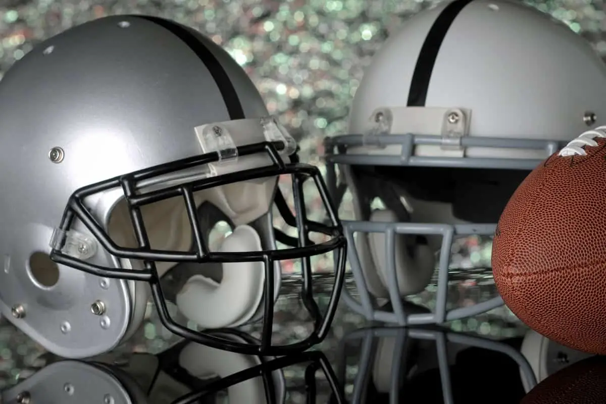 2 football helmets sitting alongside a football