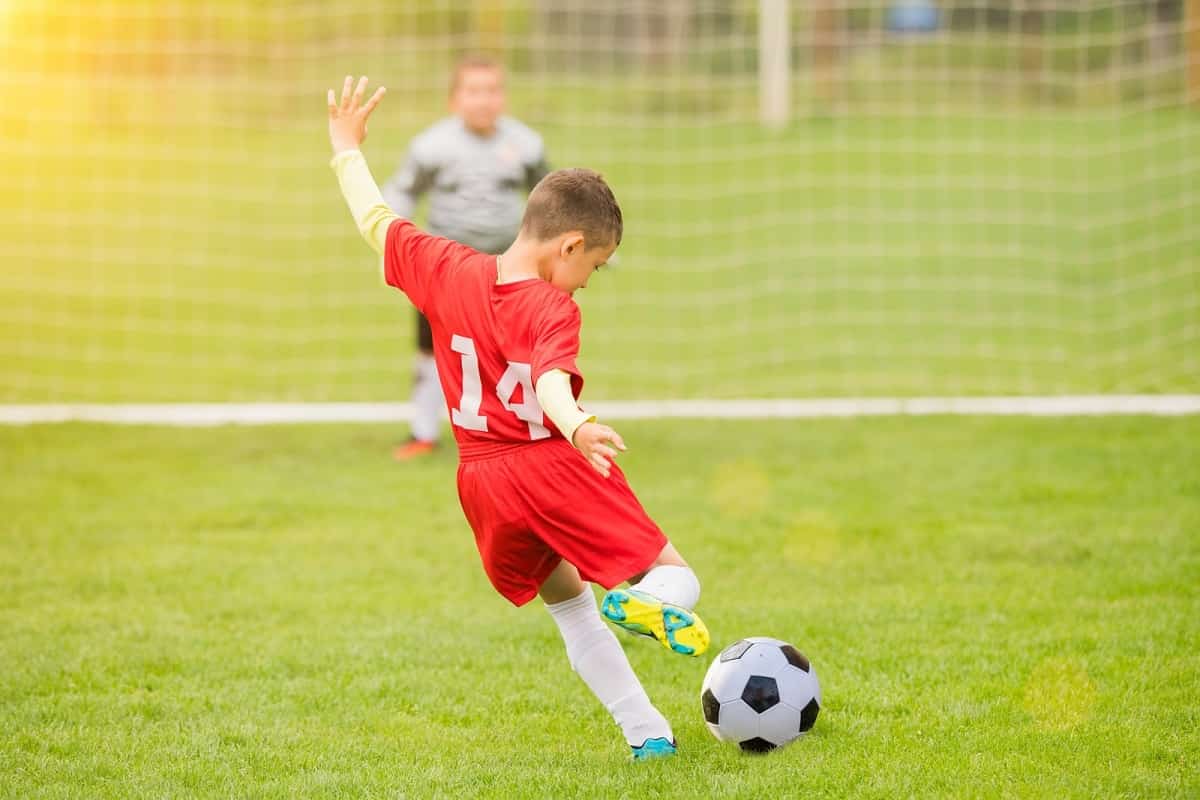 young boy in red uniform kicking for goal in soccer