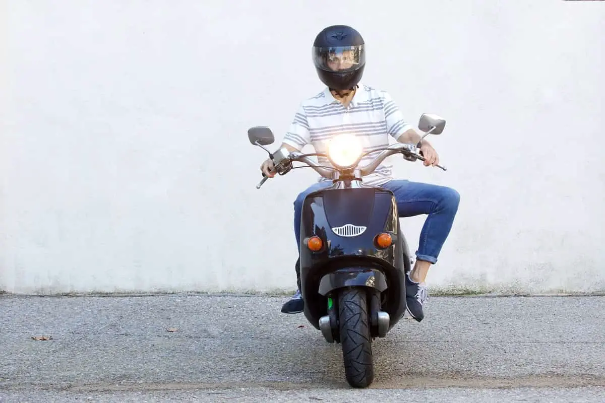 man wearing black full face motorcycle helmet sitting on a moped